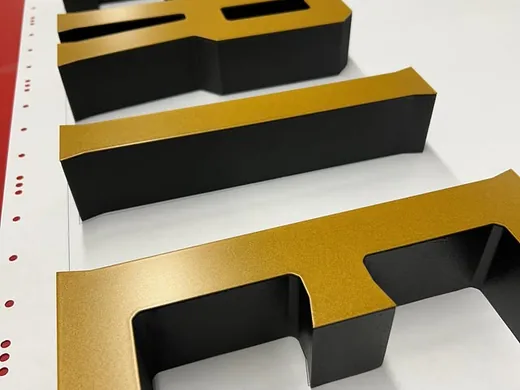 Black and gold dimensional letters photographed from the side to show depth and edge finish