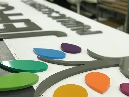Colorful layered logo pieces and gray dimensional letters prepared for assembly