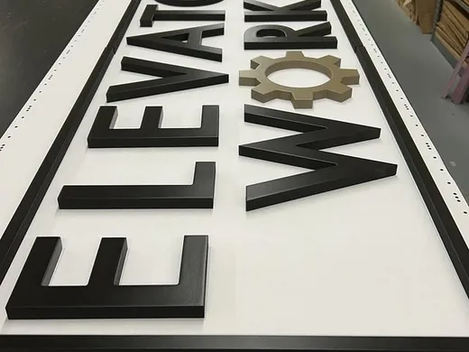Black dimensional letters and gear logo arranged for an Elevator Works sign