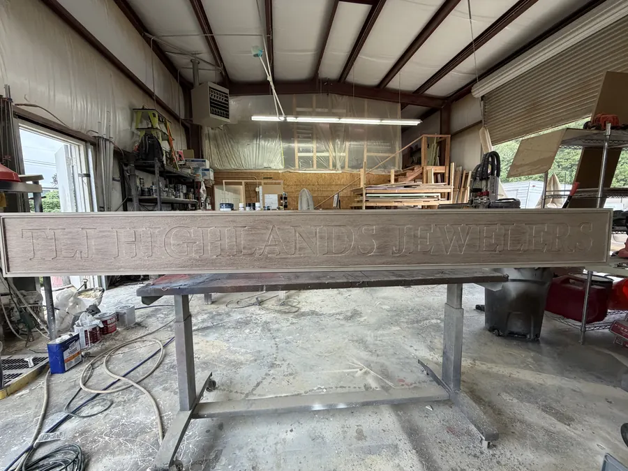 Long routed sign panel with carved woodgrain texture and raised lettering on shop supports