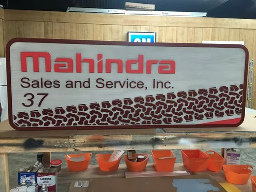 Mahindra Sales and Service dimensional sign with woodgrain background and routed tire-track detail