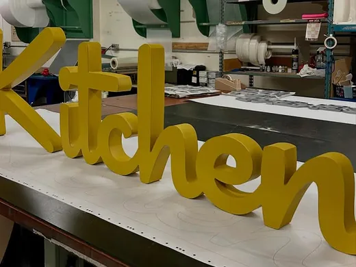 Yellow script dimensional letters arranged on a sign production table